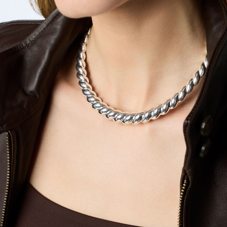 A person wearing the Ravello silver collar necklace with a twisted rope design and a brown jacket.