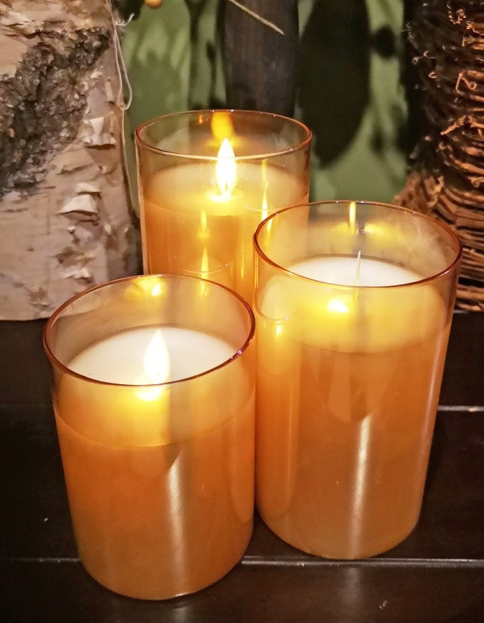 Three amber-colored glass pillar candles of varying heights with glowing LED flames.