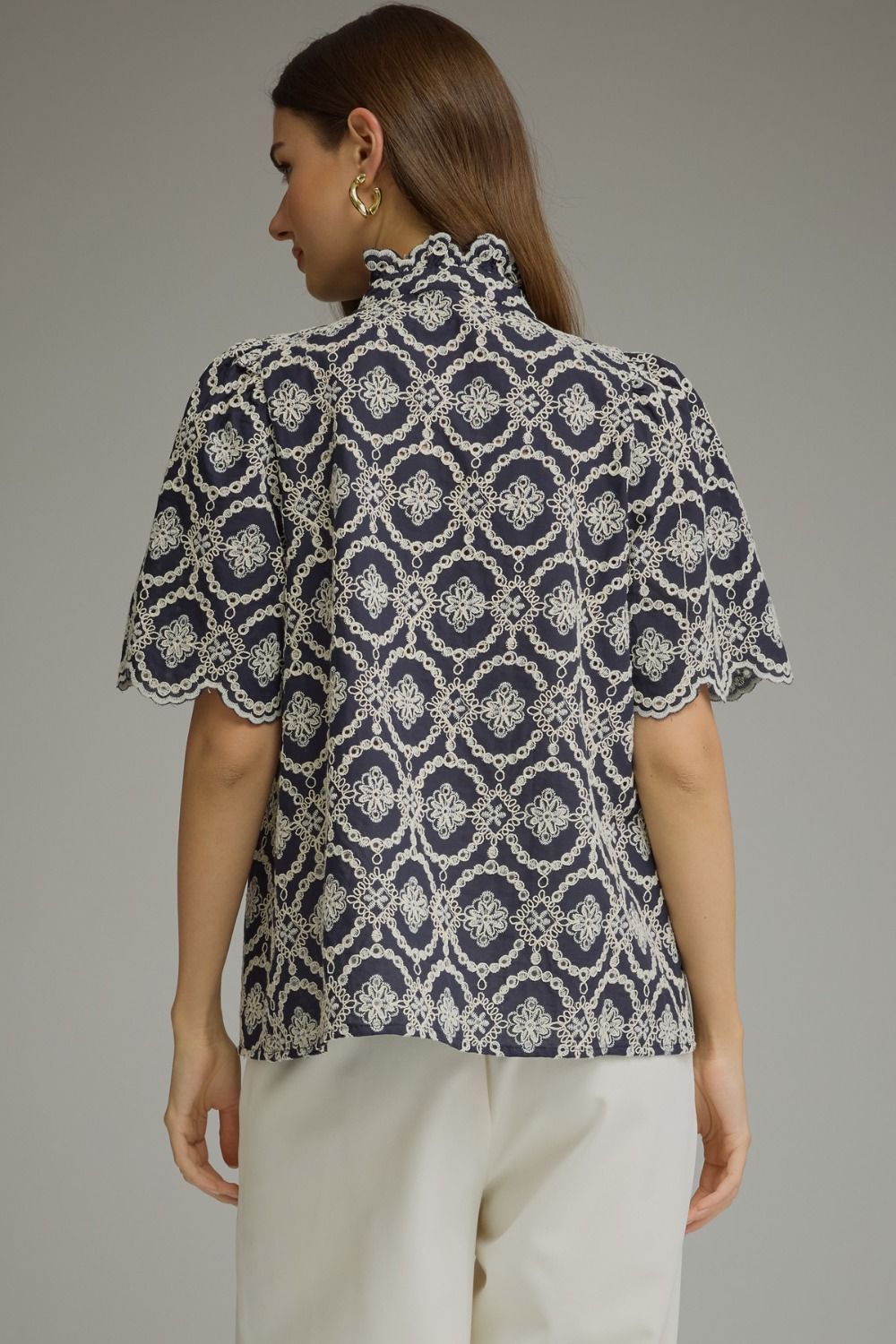 Back view of a navy Amalia top with white geometric embroidery, puff sleeves, and a ruffled collar.