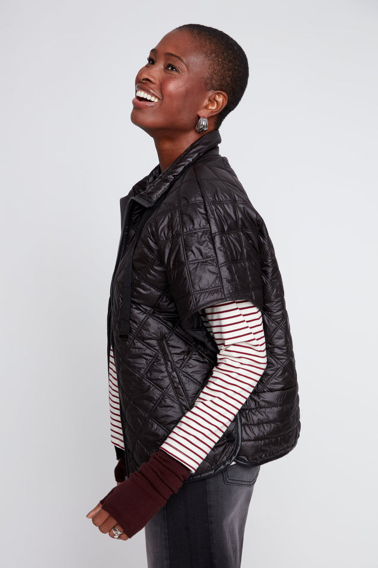Side view of a woman wearing a black Megan Luxe Quilted Poncho over a striped long-sleeve shirt.