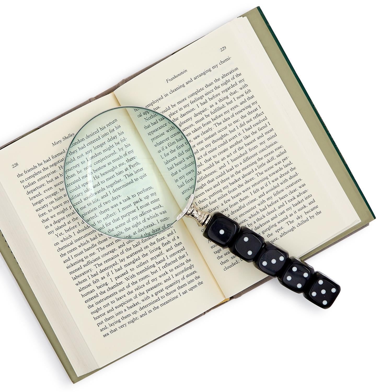 Magnifier with a black dice-shaped handle resting on an open copy of the book Frankenstein.