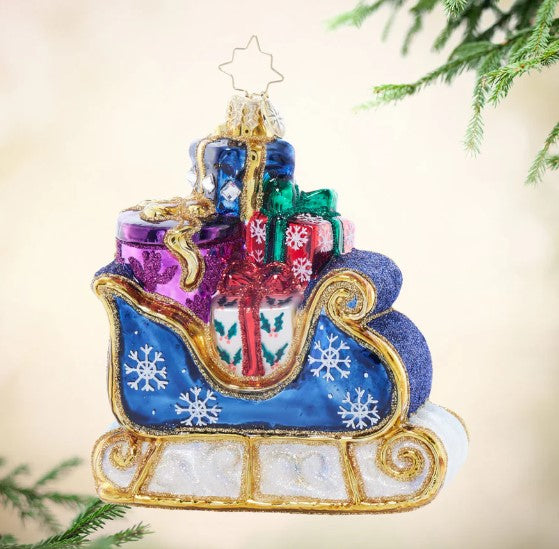 Glass Christmas ornament of a blue sleigh with gold trim, snowflakes, and colorful gift boxes.