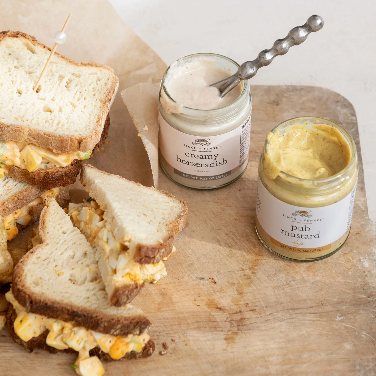 9.25 oz. jar of Finch + Fennel Creamy Horseradish Sauce next to egg salad sandwiches and mustard.