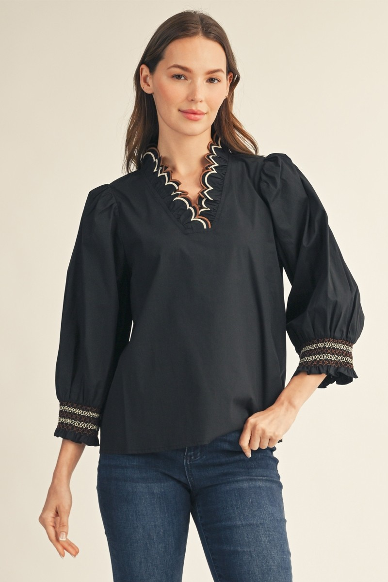 Woman in a black 3/4 puff sleeve top with an embroidered scallop V-neckline and smocked cuffs.