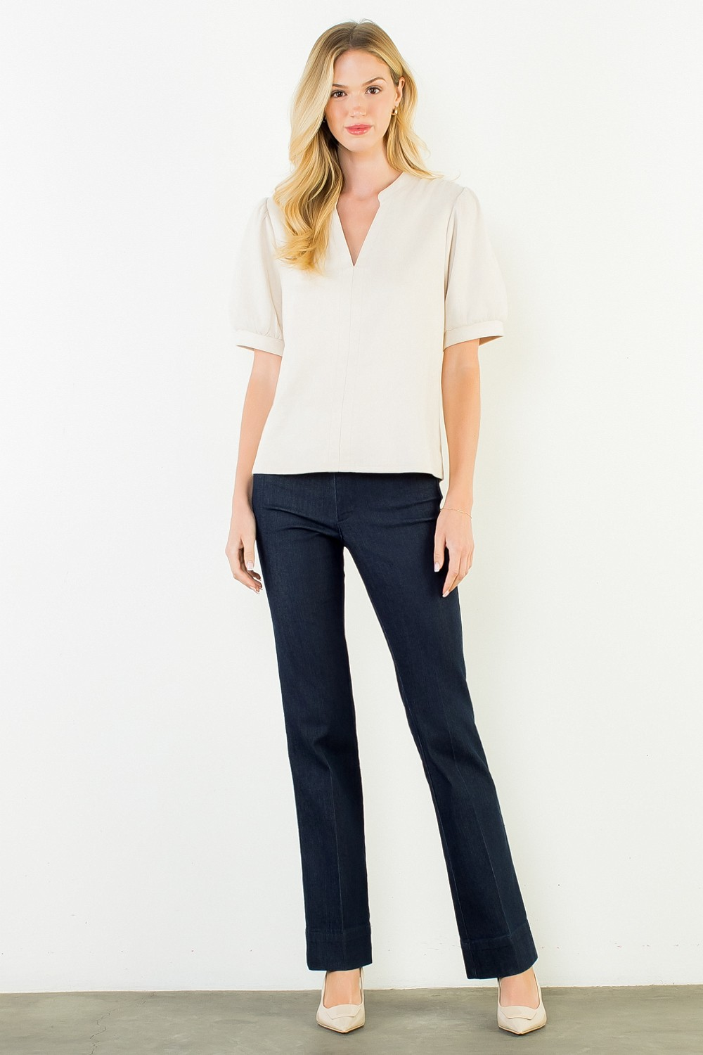 Woman wearing a cream Juliana Soft Suede V-Neck Top with short puff sleeves and dark denim trousers.