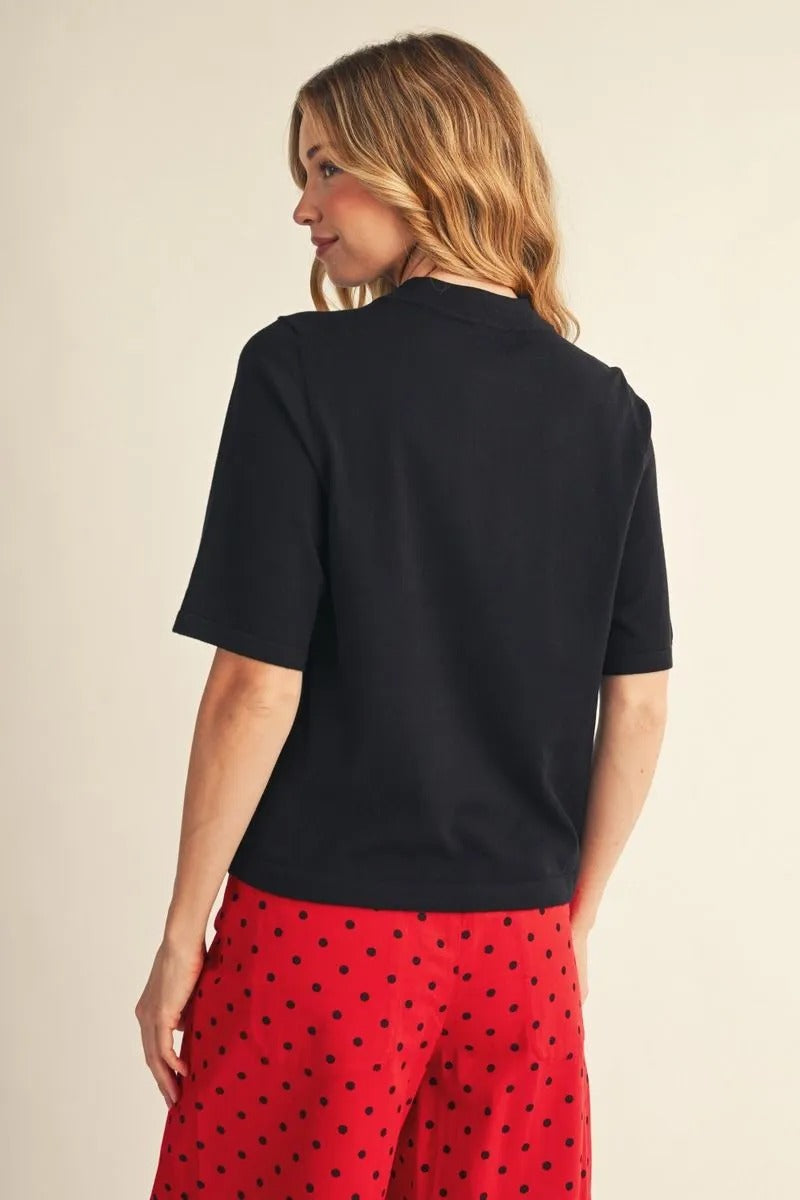 Back view of a woman wearing a black Abigail half-sleeve round neck sweater top with red pants.