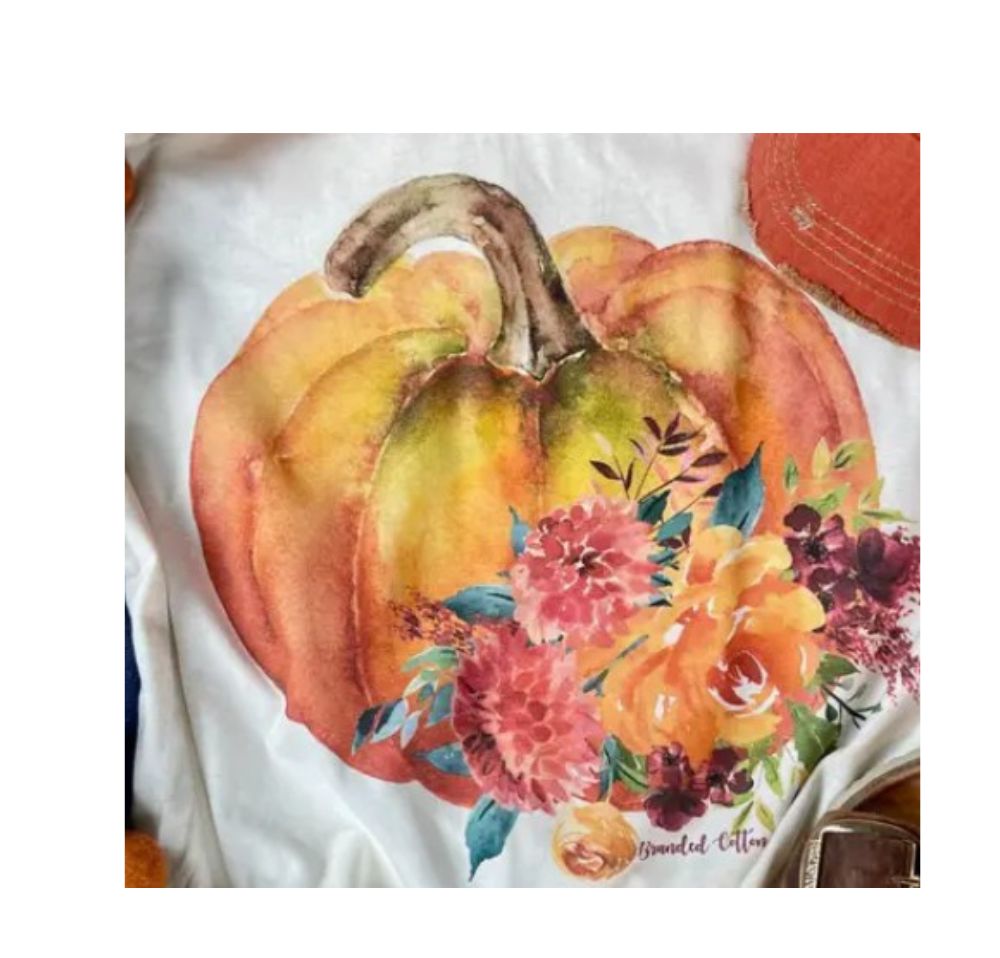 White t-shirt featuring a watercolor orange pumpkin design with vibrant pink and yellow flowers.