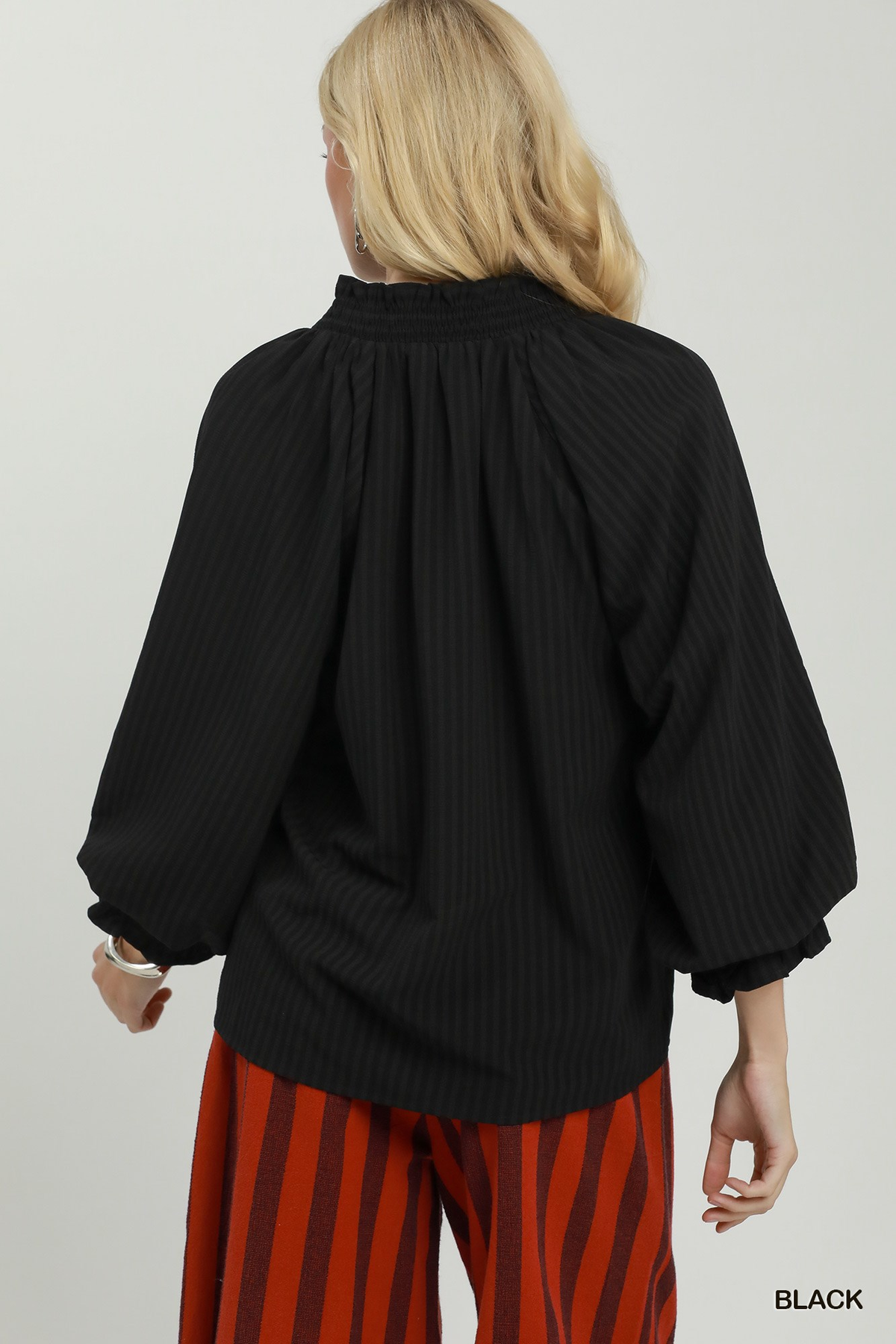Back view of a woman wearing the black Emma Stripe Split Neck Blouse with voluminous long sleeves.