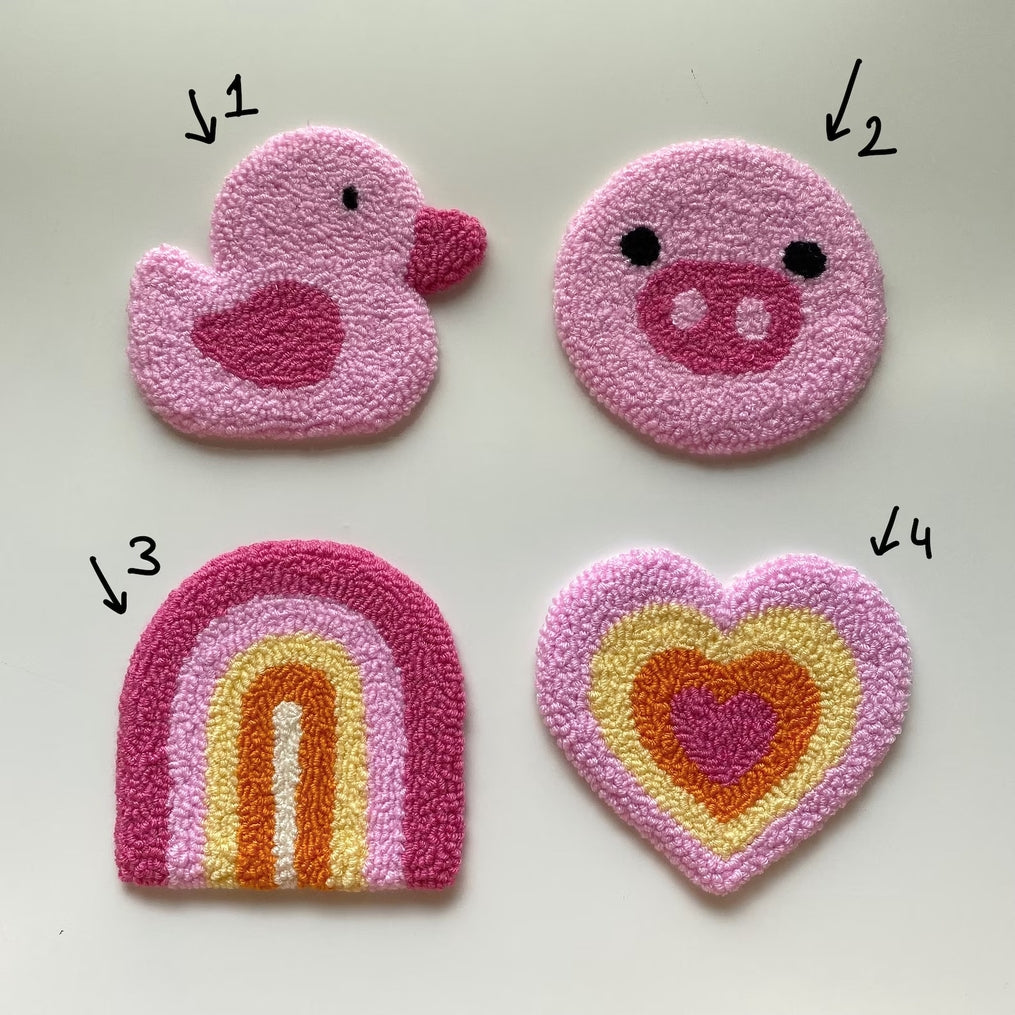 Four handmade punch needle coasters: a pink duck, a pig face, a rainbow, and a layered heart.