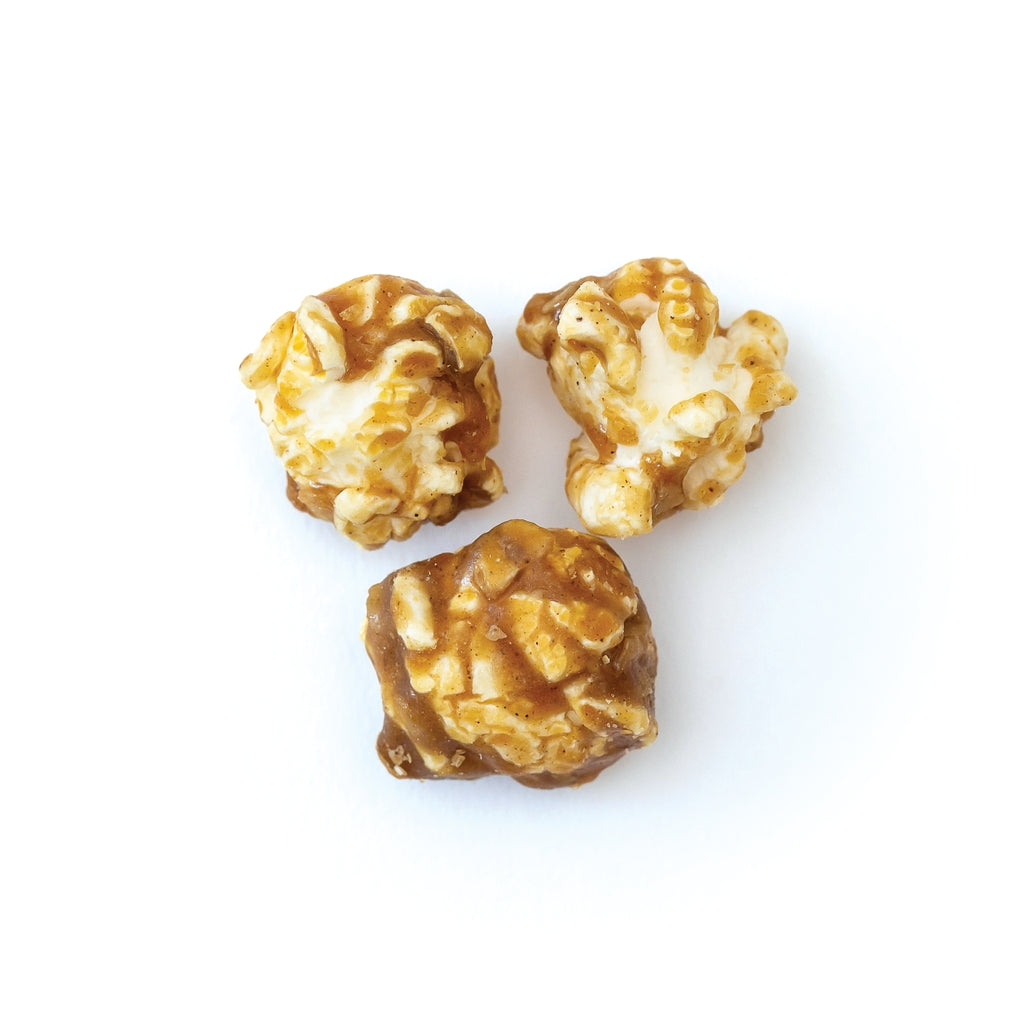 Three pieces of oatmeal cookie popcorn coated in cinnamon caramel and rolled oats on a white surface