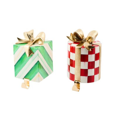 Two gift-shaped stocking holders: one green striped cube and one red checkered cylinder with bows.