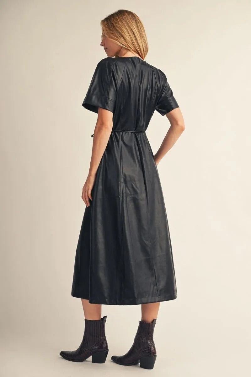 Back view of a woman wearing the Allison black short-sleeve faux leather midi dress with boots.