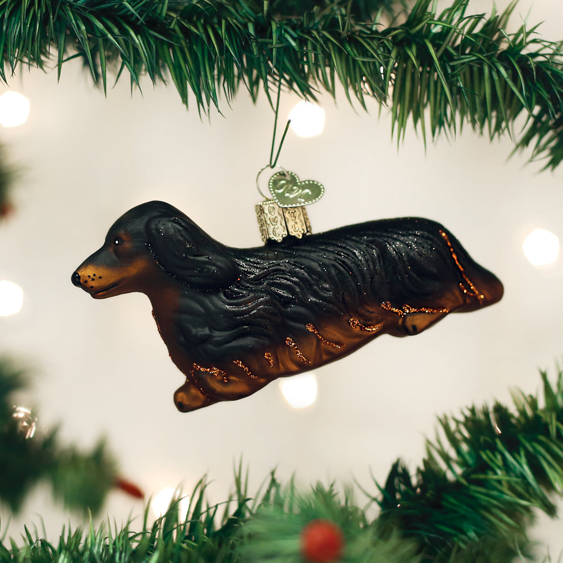 Glass long-haired dachshund ornament with black and tan fur hanging on a Christmas tree.