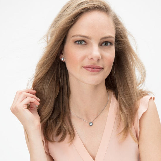 Woman wearing a Twinkle Crystal Necklace with a silver-plated round pendant and matching earrings.