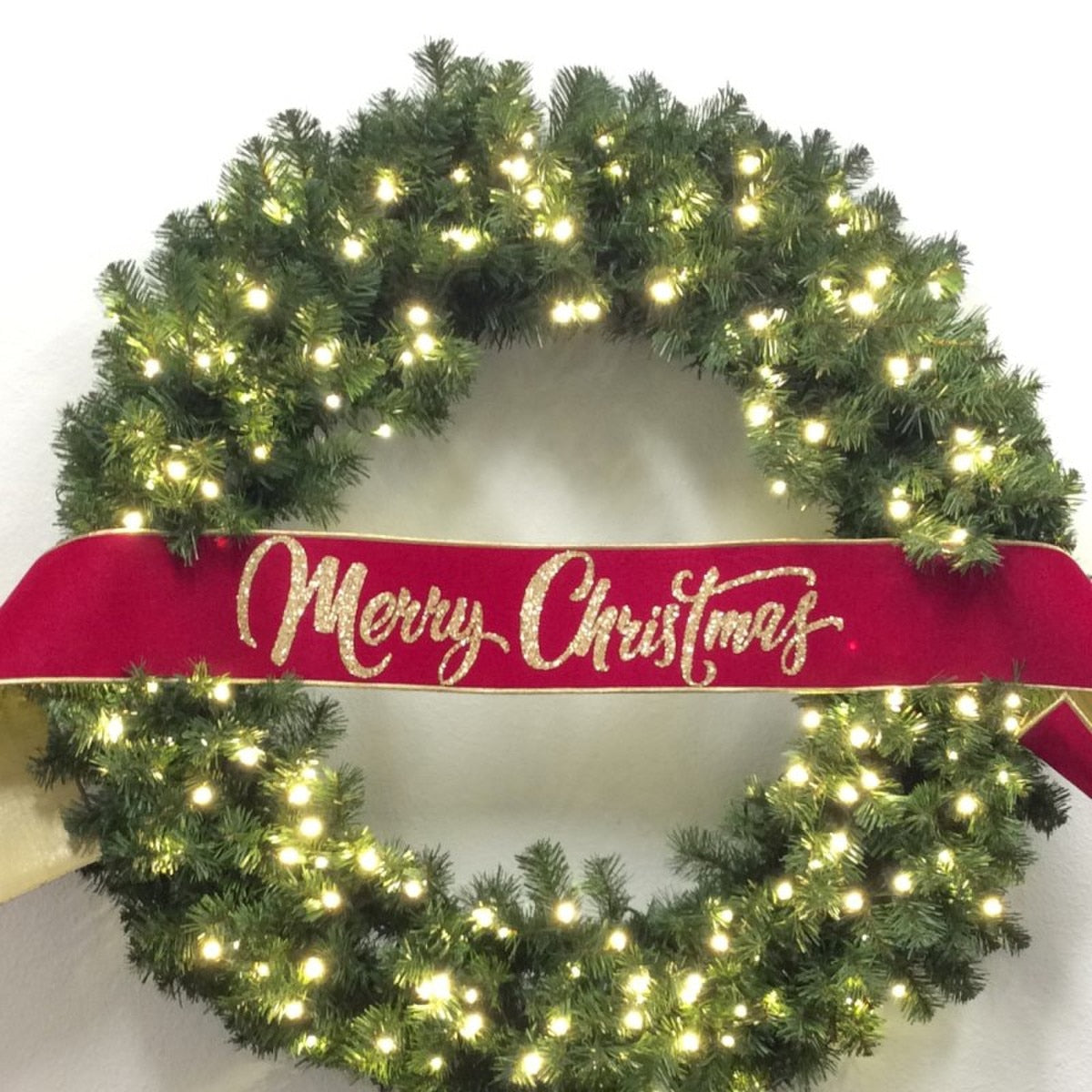 Hot pink velvet banner with gold glitter "Merry Christmas" text draped across a lighted wreath.