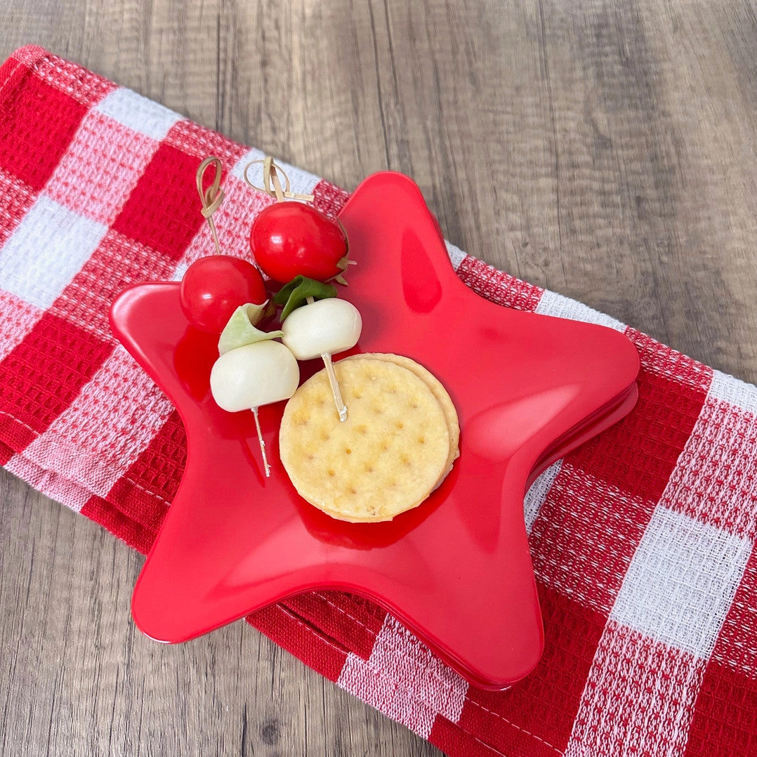 Holiday red 8-inch melamine star-shaped plate with a cracker and caprese skewers on a red cloth.