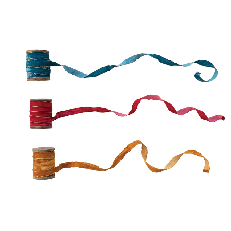 Three velvet ribbons in blue, red, and gold with metallic edges on mango wood spools.
