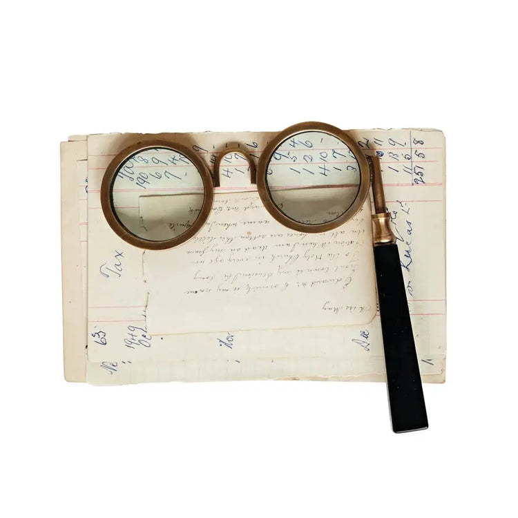 Antique-style magnifying spectacles with a circular lens on a decorative frame.