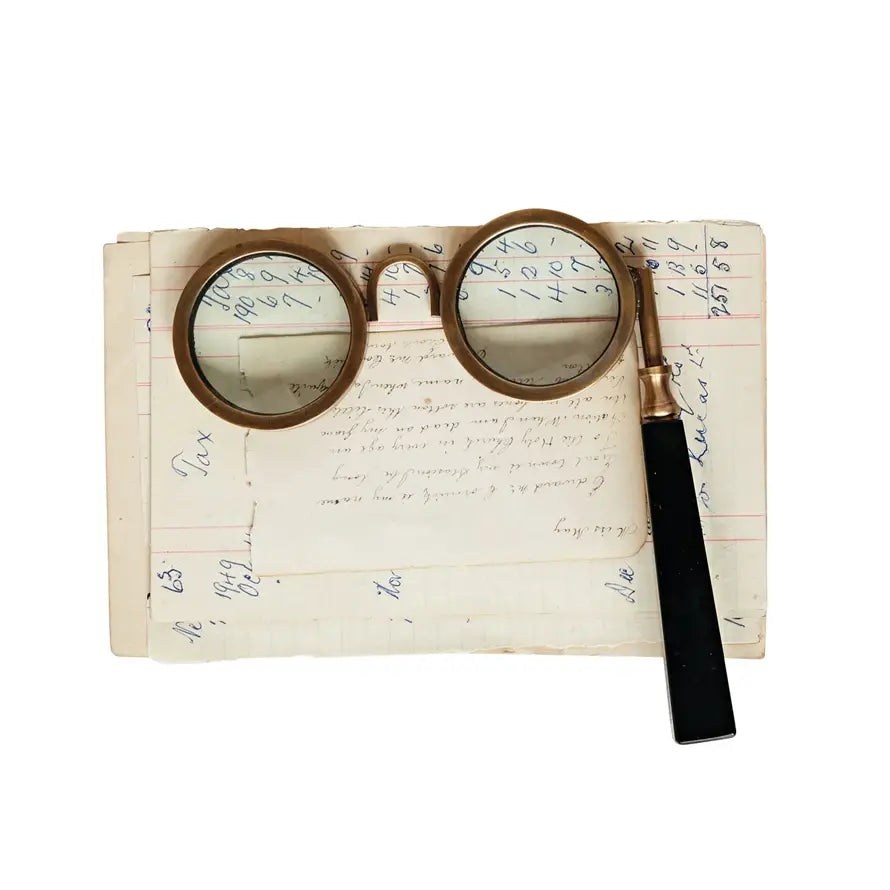 Antique-style magnifying spectacles with a circular lens on a decorative frame.