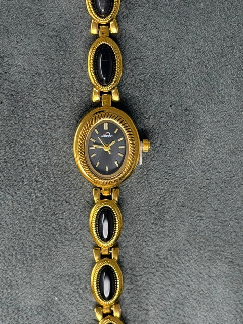 Oval goldtone watch with a black face and a link bracelet featuring black oval stones.