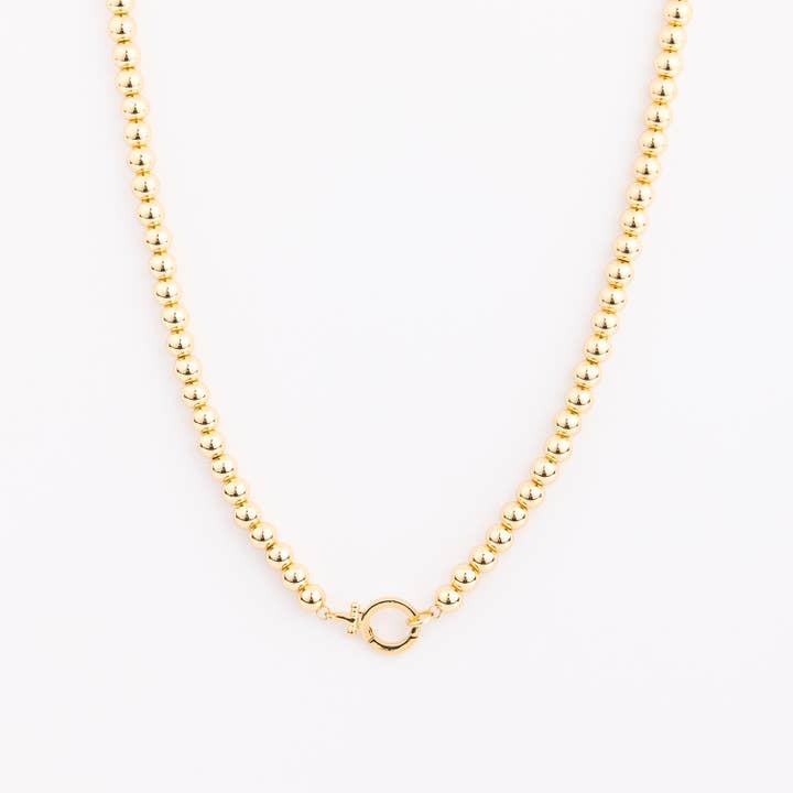 Gold beaded necklace with large spherical beads and a circular toggle clasp on a white background.