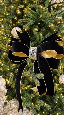 Black velvet holiday bow with gold trim and a rhinestone center on a Christmas tree.