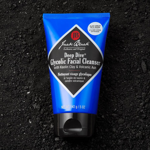 Jack Black Deep Dive Glycolic Facial Cleanser 5 oz tube on a dark, textured volcanic ash background.