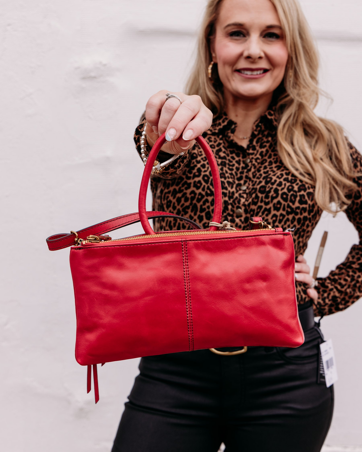 A woman holding a True Red Sable Crossbody bag with a top handle and gold zipper details.