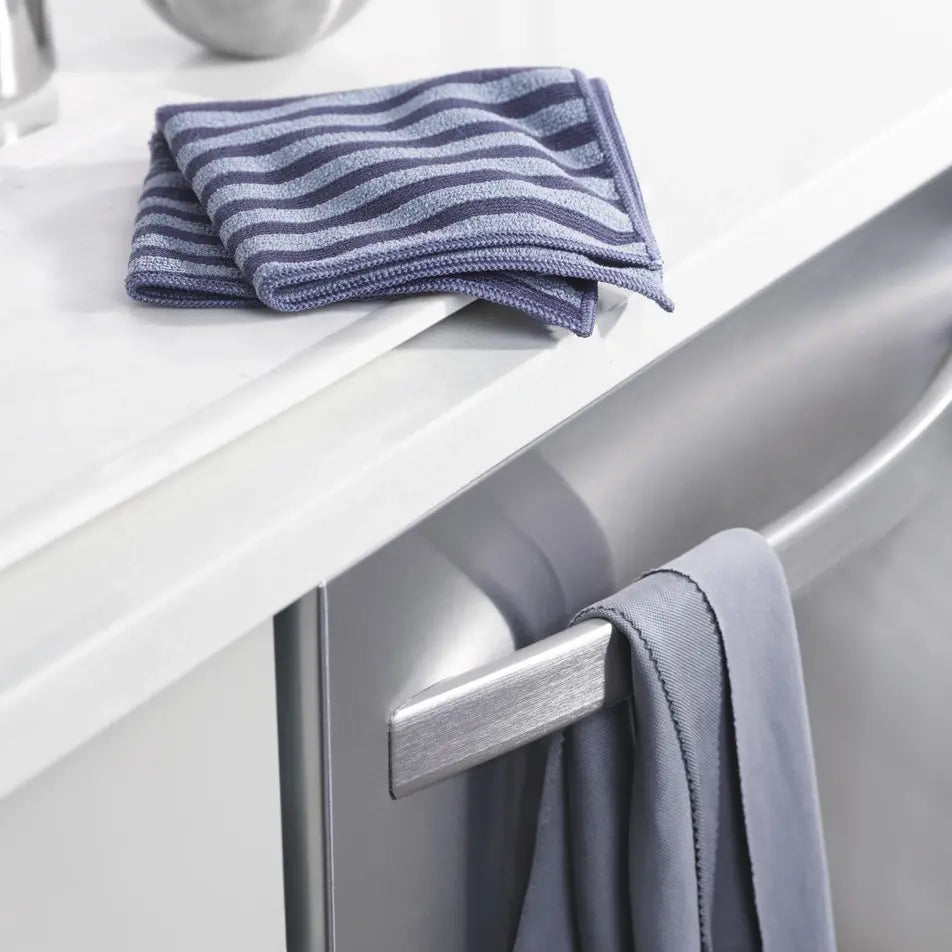 Striped stainless steel cleaning cloth and solid grey polishing cloth on a kitchen appliance.