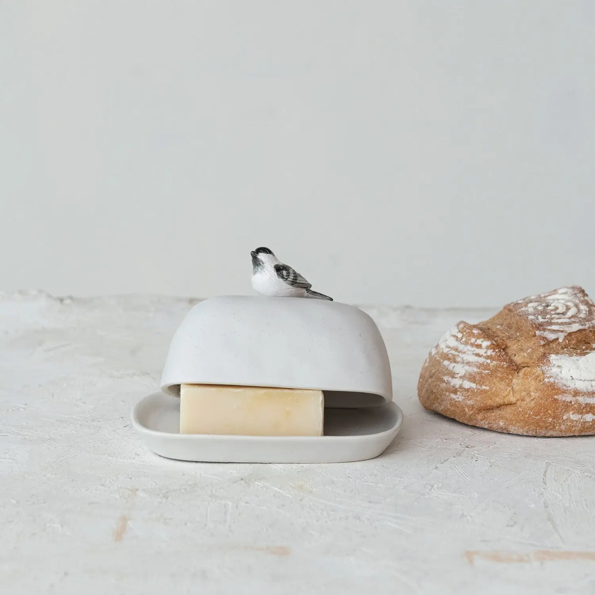 Stoneware butter dish with a bird-shaped handle in natural earth tones.