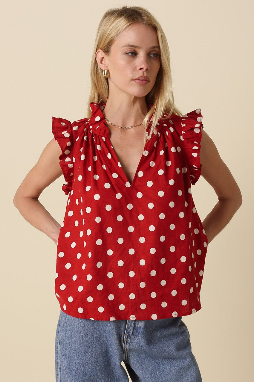 Woman wearing a red Mira Polka Dot Ruffle Blouse with white dots and sleeveless ruffle shoulders.
