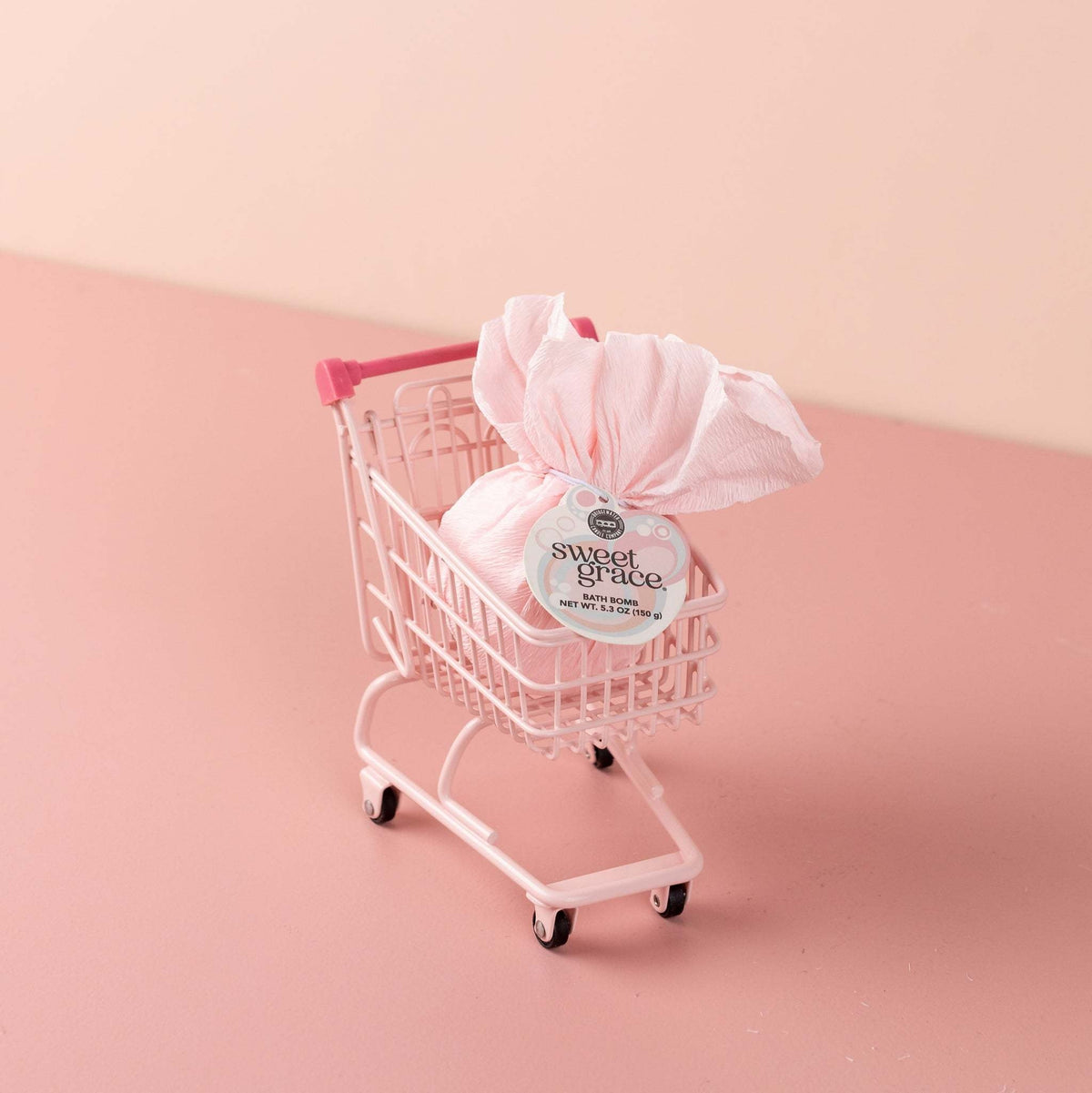 Round Sweet Grace bath bomb in pastel pink with white speckles