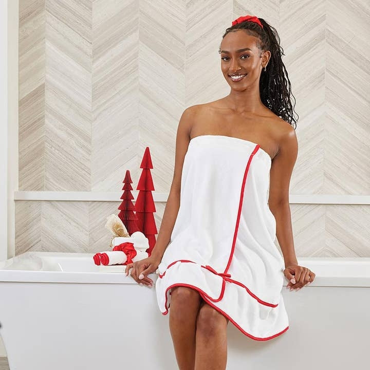 Woman wearing a white spa wrap with red trim sitting on the edge of a bathtub.