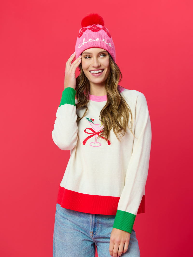 Woman in a white Martini Lightweight Boxy Sweater with red and green trim and a pink beanie.
