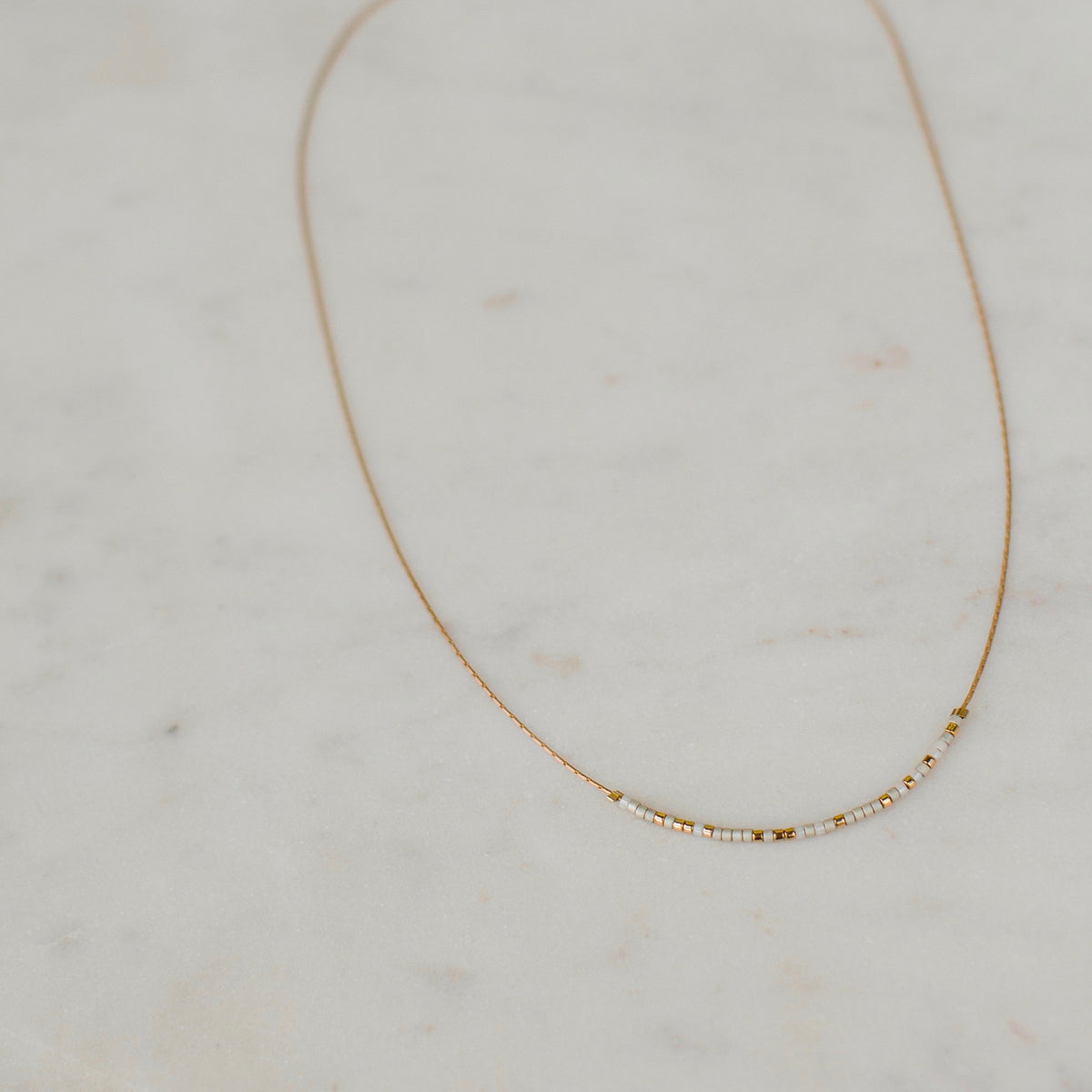 Be the Change Necklace featuring a thin gold chain with small white and gold beads.