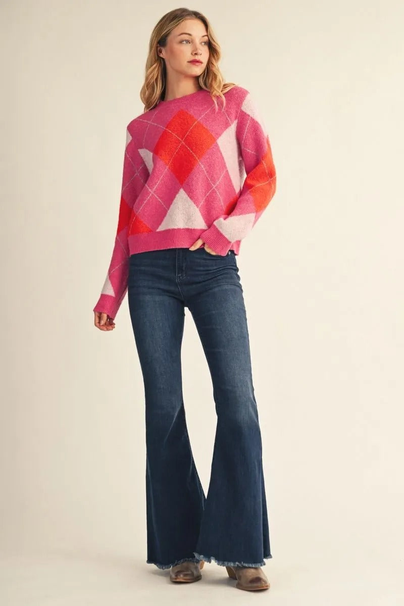 Woman wearing a pink and orange argyle check long sleeve sweater with flare jeans.