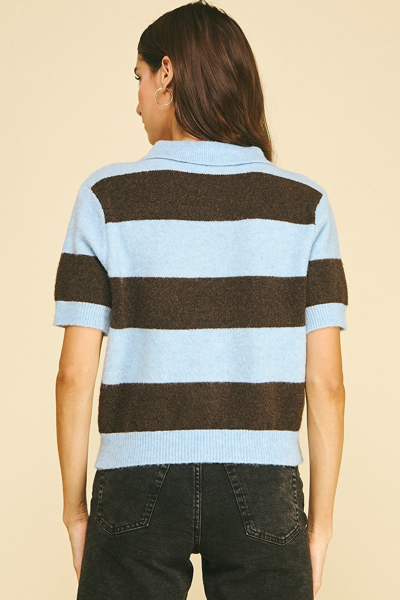 Back view of a woman wearing a light blue and brown horizontal striped short sleeve knit polo.