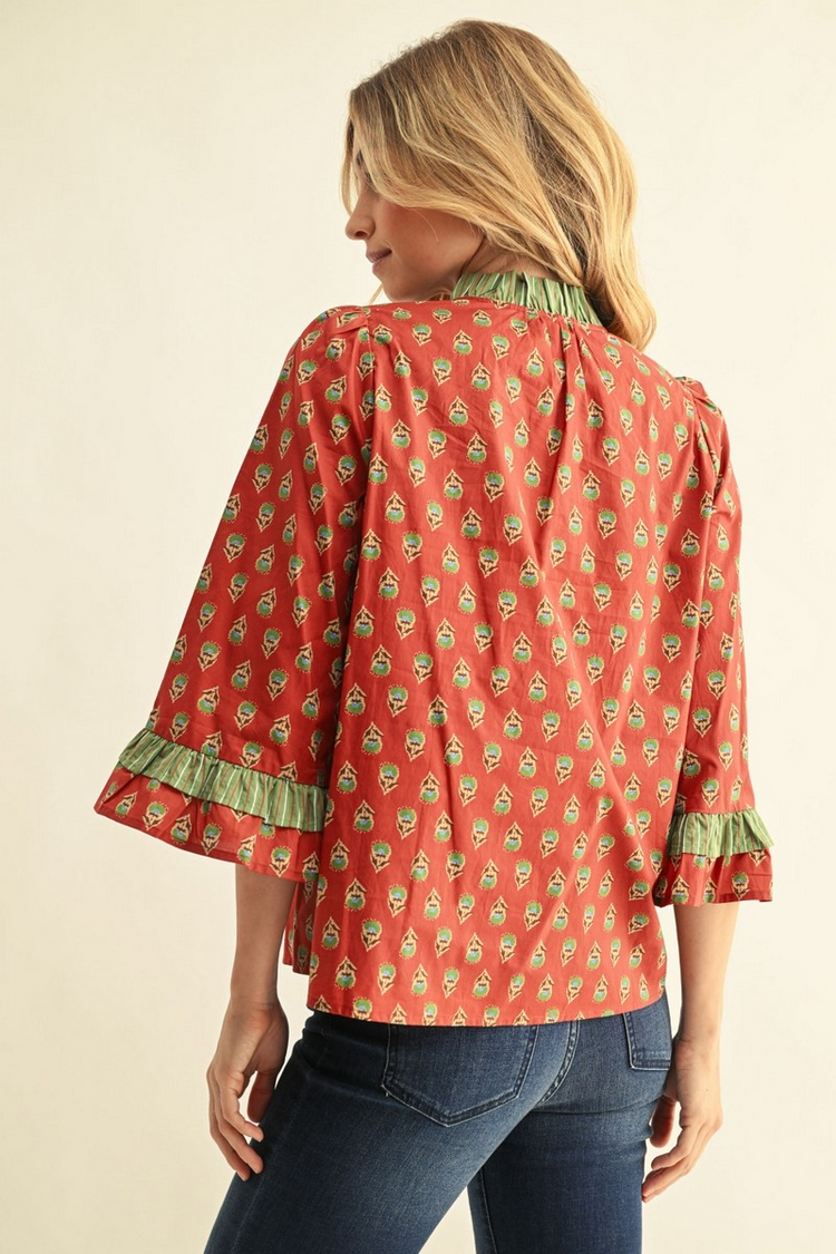 Back view of a woman wearing a red floral cotton top with 3/4 bell sleeves and green ruffle trim.