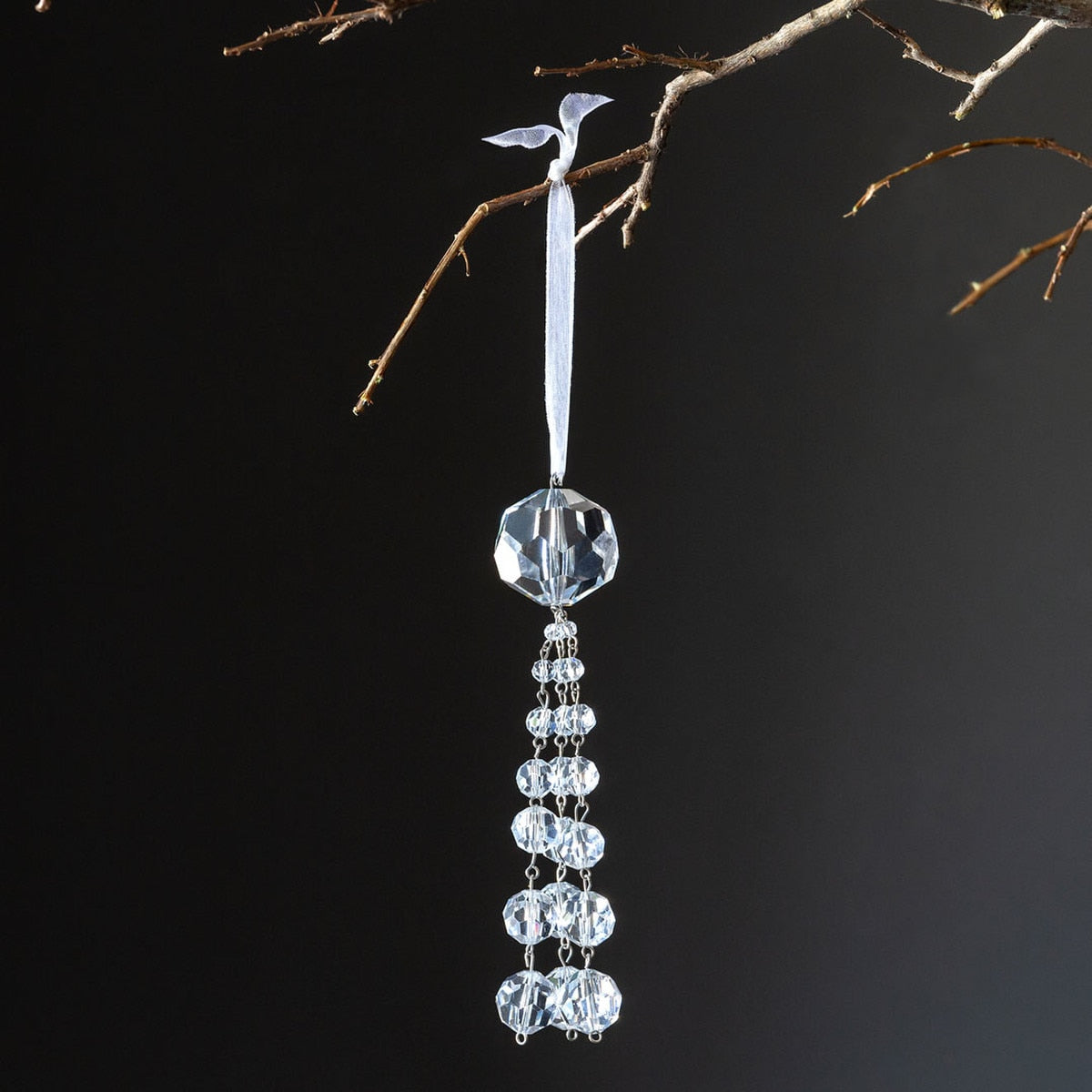 Clear glass crystal tassel ornament hanging from a branch by a white ribbon.