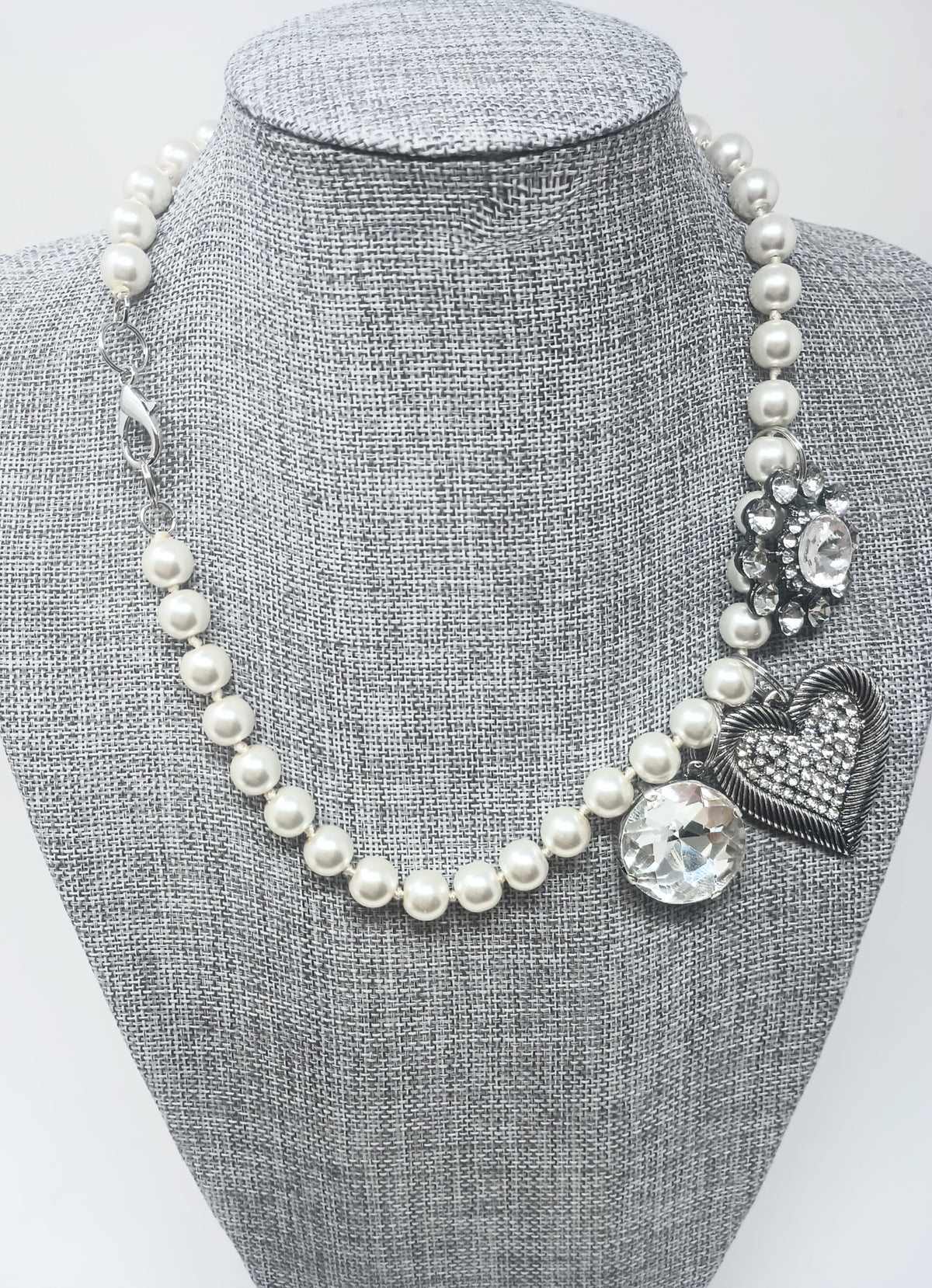 18-inch pearl necklace on a gray bust featuring three crystal-embellished charms and a heart.