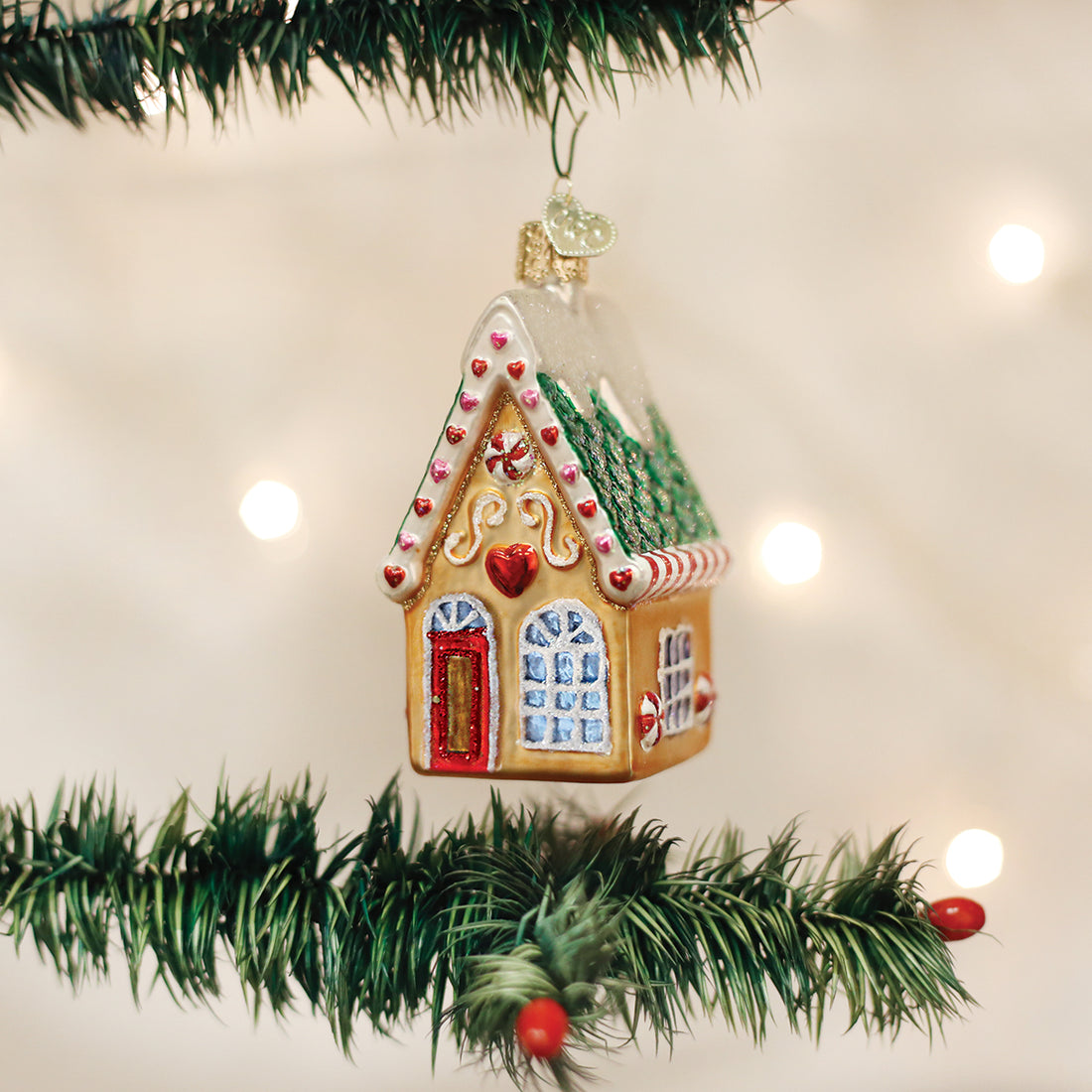Glass gingerbread house ornament with red heart and candy details hanging on a Christmas tree.