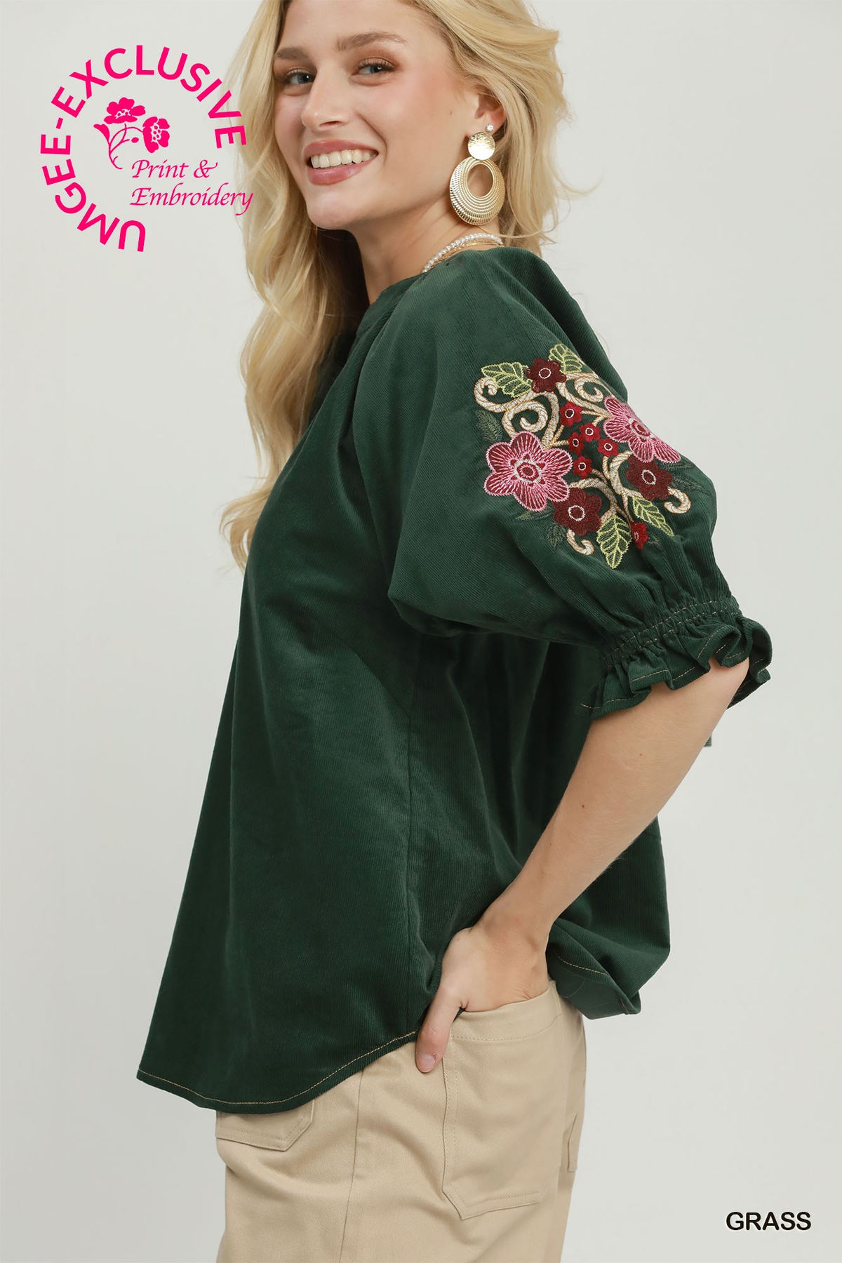 Woman wearing a dark green Eliana corduroy blouse with floral embroidery on the puff sleeves.
