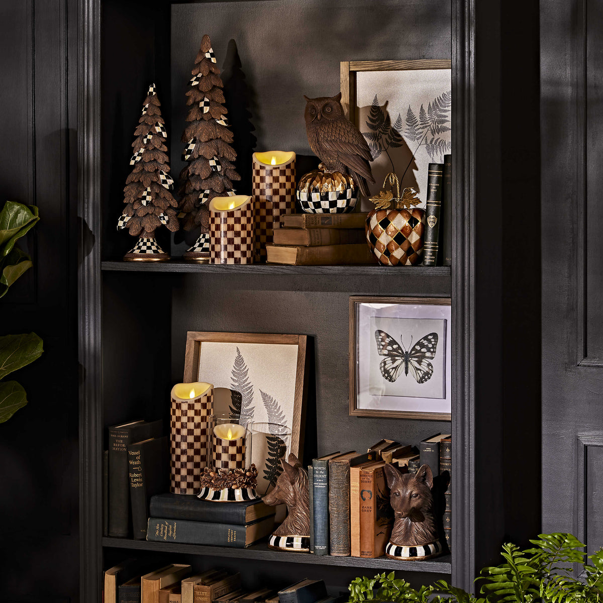 A 6-inch Courtly Check flicker pillar candle on a dark bookshelf with fall-themed decor.