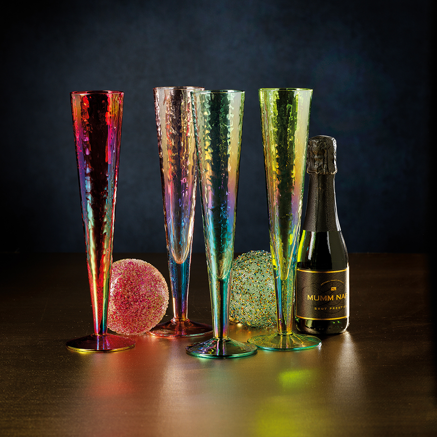 Four Aperitivo Slim Champagne Flutes in iridescent colors next to a bottle and decorative spheres.