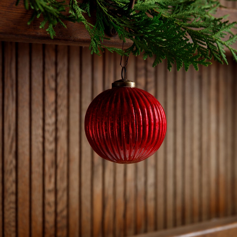 4-inch red fluted glass ball ornament hanging from a green cedar branch against a wood background.