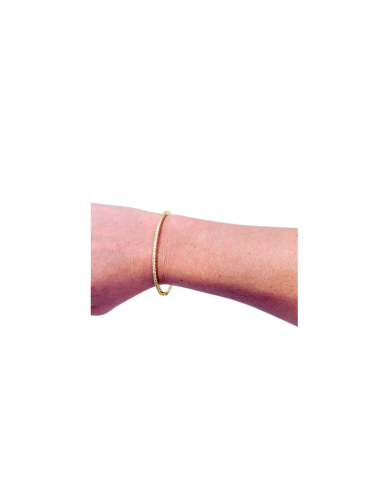 A gold-dipped hinged bangle with a row of pave-set round cubic zirconia stones on a person's wrist.