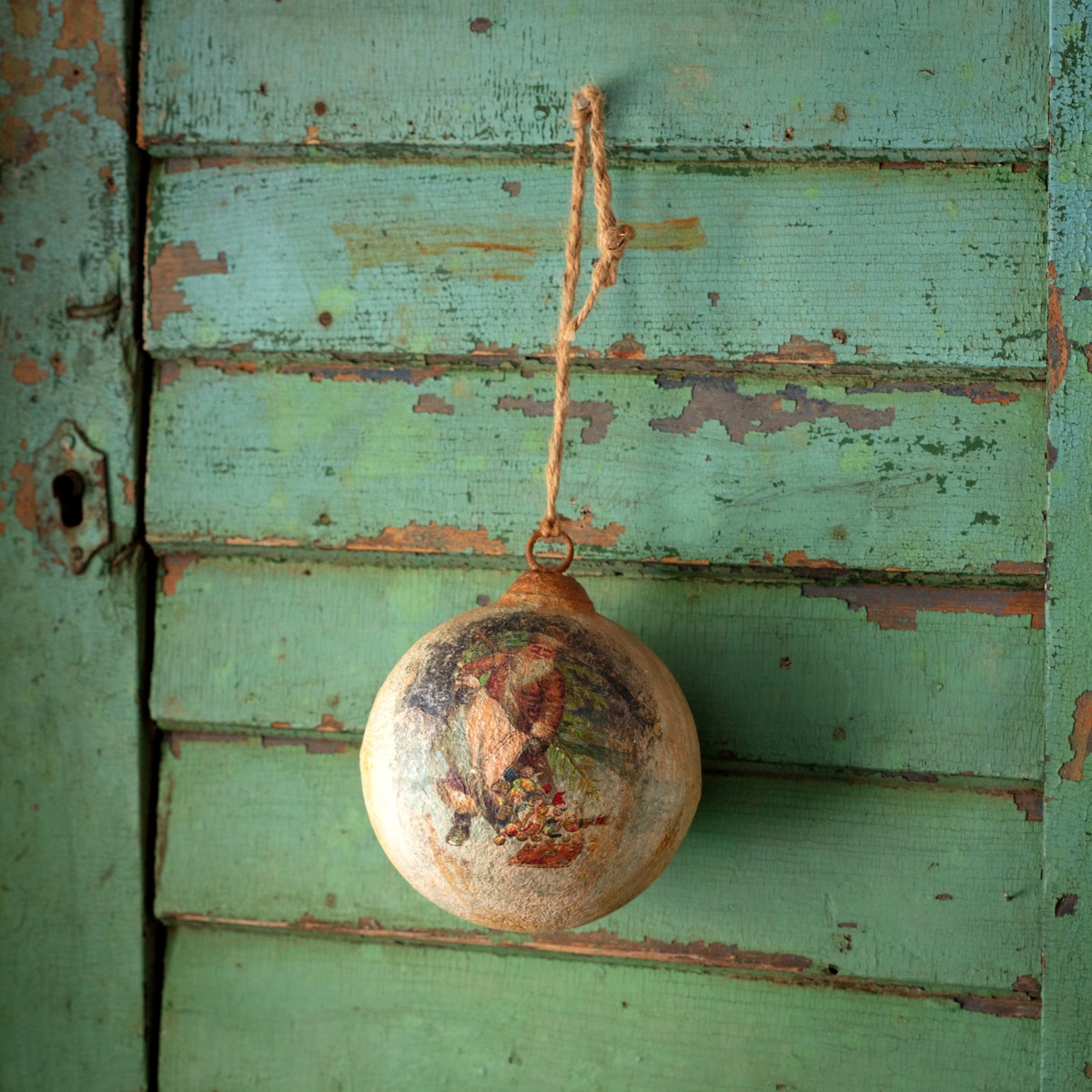 Metal ball ornament shaped like Santa holding gifts with a red finish.