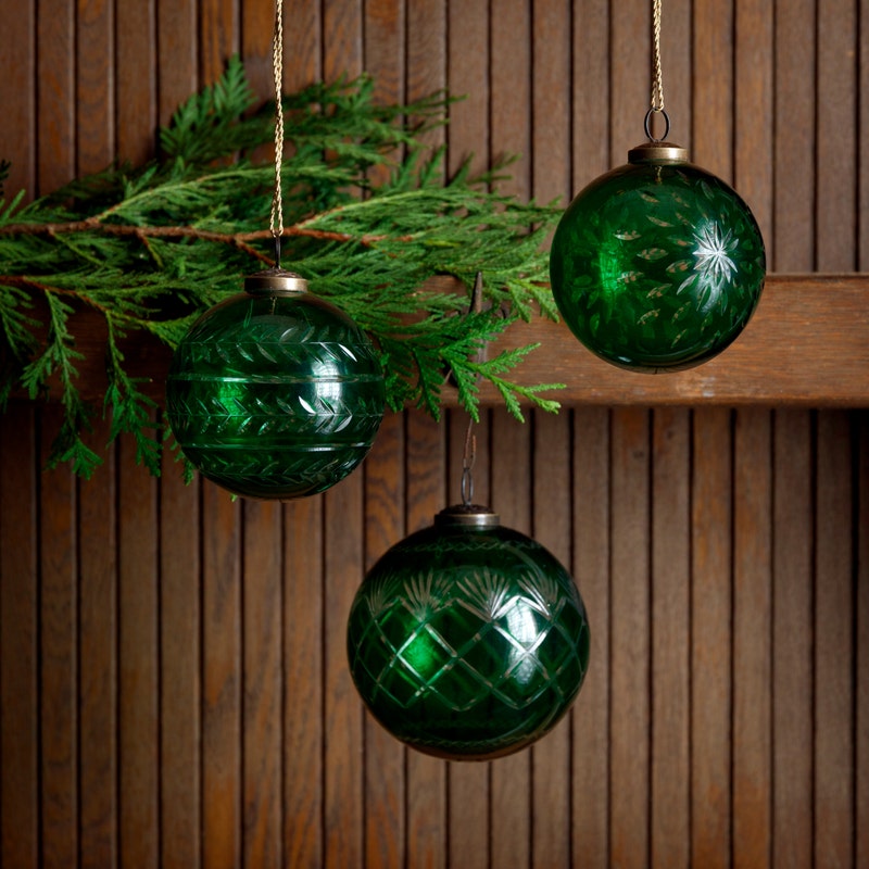 Three green cut glass ball ornaments with different patterns hanging from gold strings.