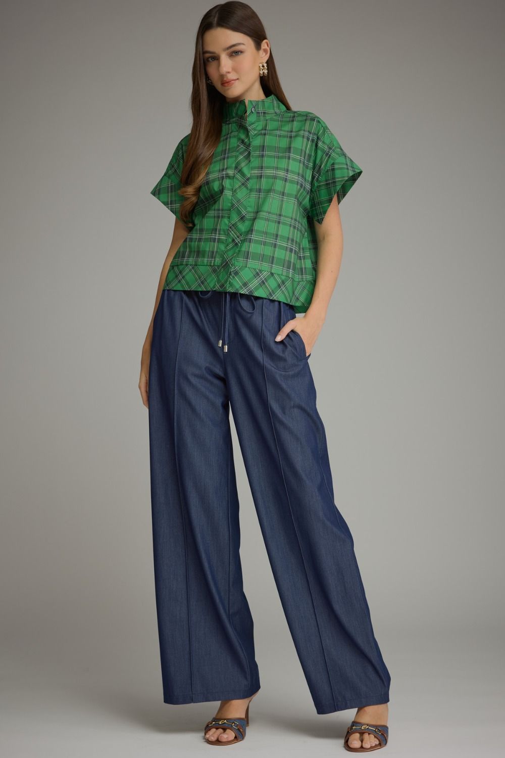 Woman wearing a green Chloe Plaid Short Sleeve Top with high neckline and wide-leg denim trousers.