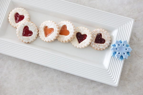 White rectangular ceramic bread tray with a striped rim, holding heart-shaped jam-filled cookies.